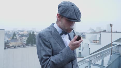 En-Este-Video-Hay-Un-Hombre-Bien-Vestido-Que-Comienza-A-Fumar-Su-Pipa-En-El-Balcón,-Mientras-Pequeños-Copos-De-Nieve-Caen-En-El-Fondo
