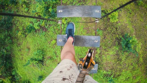 POV-Shot-Of-A-Man-Walking-On-The-High-Rope-Obstacle-With-Small-Wooden-Planks-In-The-Lush-Jungle-In-Chiang-Mai,-Thailand---high-angle