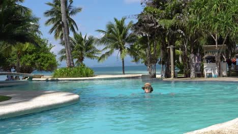 Dos-Palmas-Island-Resort,-Puerto-Princesa,-Palawan,-Philippines---Lovely-Female-Tourist-Swimming-In-A-Beautiful-Infinity-Pool-Surrounded-With-Palm-Trees-On-A-Sunny-Day---Low-Level-Shot