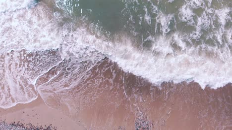 Static-aerial-looking-down-at-fast-waves-crashing-on-a-pink-sand-beach