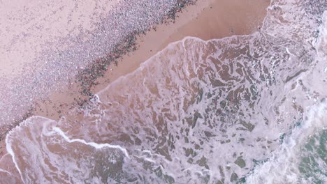 Drone-aerial-getting-close-to-waves-crashing-on-a-tropical-pink-beach-with-no-one-around