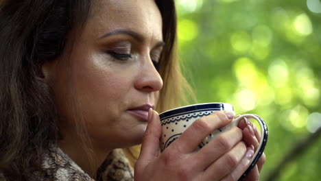 Close-up-FHD-shot-of-a-brunette-middle-aged-woman-tasting-a-cup-of-fresh-hot-tea-in-the-morning-and-slowly-opening-her-eyes