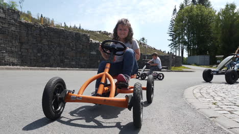 Dolly-FHD-shot-of-a-small-girl-cycling-on-an-orange-pedal-quadricycle-in-a-private-resort-in-Dolní-Morava,-Czech-Republic,-with-other-kids-cycling-behind