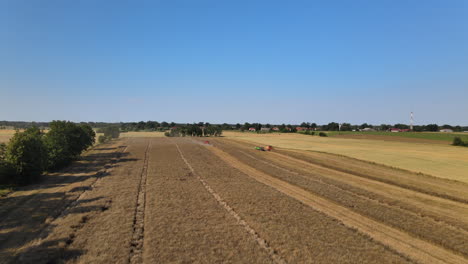 Aerial-forward-flight-showing-Combine-tractor-harvesting-farmland-during-blue-sky