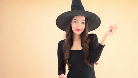 Feliz-Mujer-Bastante-Asiática-Posando-Para-La-Cámara-En-Vestido-Negro-Y-Sombrero-De-Mago-De-Bruja