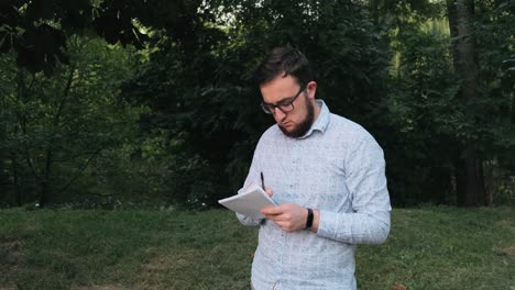 Man-with-glasses-writes-in-notebook-in-the-park
