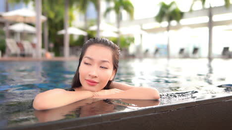 Close-up-of-an-attractive-woman-resting-her-chin-on-her-arms-while-leaning-on-the-edge-of-a-resort-swimming-pool