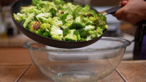 Carefully-shaking-a-pan-full-of-freshly-cooked-broccoli-into-a-glass-bowl---slow-motion