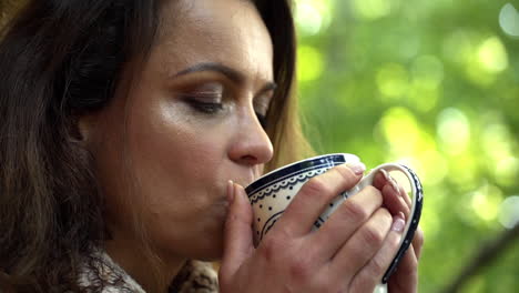 Close-up-FHD-shot-of-a-middle-aged-woman-holding-a-cup-with-both-hands-and-enjoying-a-cup-of-hot-tea-for-breakfast,-slowly-opening-her-eyes