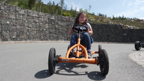 Slow-motion-FHD-shot-of-a-small-girl-cycling-on-an-orange-pedal-quadricycle-in-a-private-resort-in-Dolní-Morava,-Czechia,-while-other-kids-are-cycling-behind