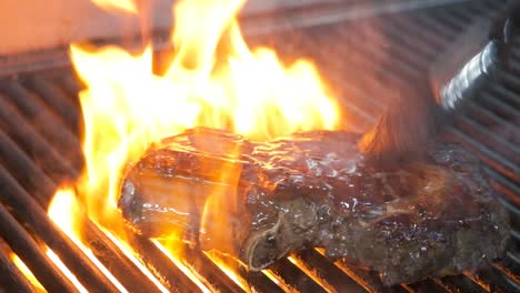 Close-up-of-flipping-a-juicy-steak-on-the-BBQ-and-brushing-on-sauce-as-the-flames-rise-on-the-grill