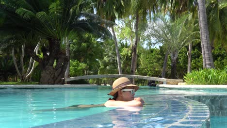 Girl-Wearing-A-Hat-And-Sunglasses-Relaxing-And-Leaning-On-The-Edge-Of-A-Swimming-Pool-In-Dos-Palmas-Island-Resort-And-Spa-In-Puerto-Princesa,-Palawan,-Philippines