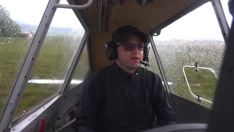 Statische-FHD-Nahaufnahme-Eines-Männlichen-Piloten,-Der-In-Einem-Cockpit-Sitzt,-Sein-Kopfhörerset-Einstellt-Und-Auf-Ein-Startzeichen-Von-Einem-Feldflughafen-Wartet