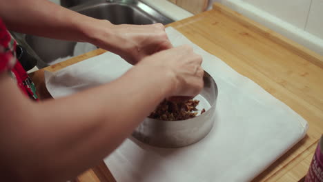 Woman-puts-vegetarian-fruits-and-nuts-mixture-into-a-circular-baking-pan
