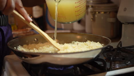 Pouring-chicken-broth-over-rice-and-stirring-in-the-steaming-homemade-stock---slow-motion
