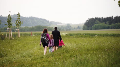 Static-scenic-FHD-shot-of-a-family-with-two-daughters-hiking-through-a-picturesque-countryside-in-Dolní-Morava,-Czech-Republic-with-a-misty-horizon-in-the-backround