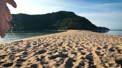 Hand-Dripping-Sand-On-The-Scenic-Sandbar-Of-Mae-Haad-Beach-In-Koh-Phangan,-Thailand---close-up-slowmo