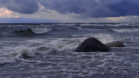 Waves-in-the-sea-during-a-thunderstorm-at-sunset,-large-stones-on-the-sea-shore