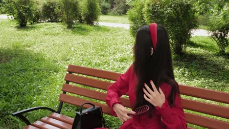 Girl-in-red-sits-on-a-park-bench-and-combs-her-hair