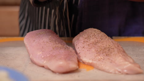 Peppering-skinless,-boneless-chicken-breasts-using-a-grinder-in-preparation-for-cooking-them
