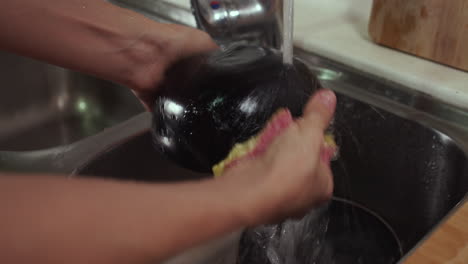 Woman-washes-black-bowl-under-tap-water-in-a-sink