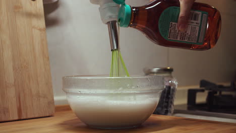 Woman-adds-honey-while-electronic-whisk-mixes-cake-batter-in-glass-bowl