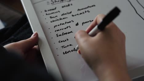 Woman-writing-shopping-list-on-white-board-with-black-marker