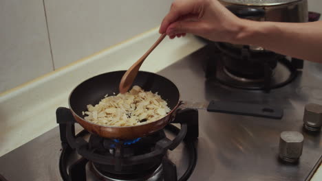 Woman-hand-stirring-almond-nuts-fried-in-a-metal-pan,-on-a-gas-cooking-pan