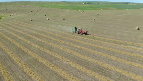 Large-dry-pasture-in-America-with-tractor-making-bales-of-hay,-aerial-circle-pan