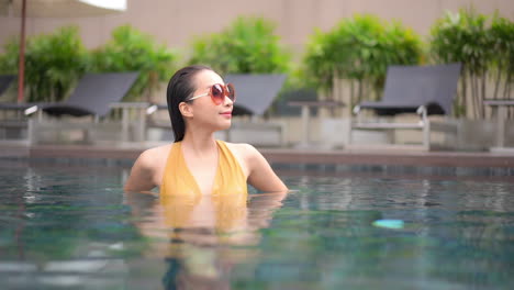 An-attractive-woman-chest-high-in-a-high-end-resort-swimming-pool-adjusts-her-sunglasses