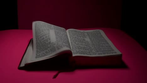 Open-bible-laying-on-bright-pink-surface-with-pages-blowing-in-the-wind