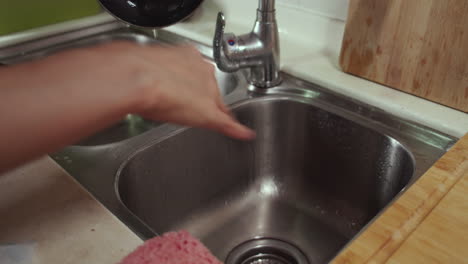 Woman-washes-dirty-rusty-frying-pan-under-tap-water-in-a-sink