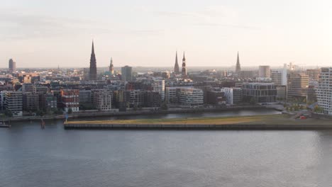 Drohnenflug-über-Hamburg-An-Einem-Sonnigen-Sommermorgen-Von-Der-Hafenseite-Mit-Dem-Neuen-Haus-Der-Elbphilharmonie,-Dem-Michel-Und-Den-Landungsbrücken-Im-Hintergrund