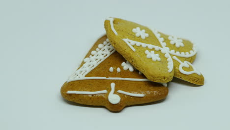 A-hand-lays-a-confectionery-gingerbread-with-white-decoration-on-top-in-the-shape-of-a-bell-and-heart-on-a-white-background