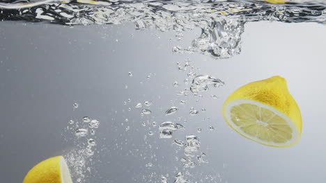 Underwater-shot-of-lemon-falling-in-water-and-splitting-in-halfs