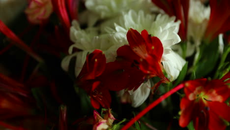 Zoomed-in-detailed-a-large-bouquet-of-red-and-white-flowers-and-green-decorative-elements-in-a-glass-vase-decorated-with-paper-around-on-a-dark-background