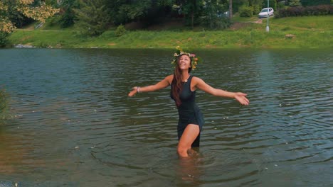 Young-Female-With-Floral-Wreath-Standing-in-Lake-Water-And-Raising-Hands-to-Sky