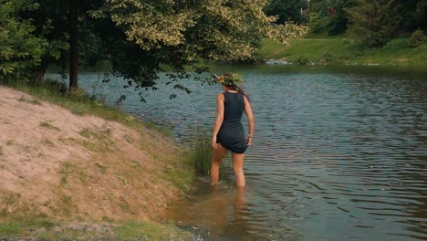 Slow-Motion-of-Attractive-Barefoot-Female-in-Dress-With-Flower-Wreath-in-Nature-Walking-in-Riverwater-and-Riverbank-Under-Tree