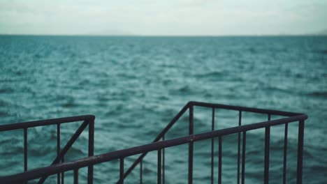 Selective-Focus-Shot-Of-Steel-Railing-By-The-Sea-With-Wave-Motion-In-The-Blurry-Background-In-Shiga,-Japan---slow-motion