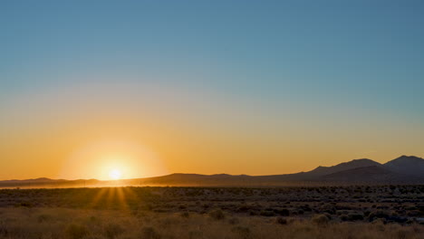 Dawn-breaks-in-this-epic-sunrise-on-a-hot,-clear-summer-morning-over-the-Mojave-Desert-landscape---grazing-herd-of-sheep-causes-dust-to-raise-in-the-distance