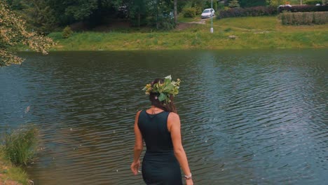 A-pretty-young-happy-girl,-wearing-black-dress,-entering-the-pond-during-outdoor-hike-in-the-forest,-woman-in-nature