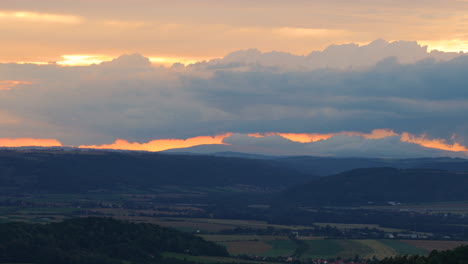 Hügelige-Landschaft-Unter-Hügeln-Voller-Bauernhöfe-Und-Felder-Bei-Sonnenuntergang-Mit-Orangefarbenen-Wolken