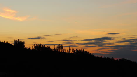 Blick-Auf-Die-Hügelkuppen,-Wo-Dunkle-Bäume-Im-Hintergrund-Von-Schatten-Und-Silhouetten-Von-Wolken-Verborgen-Sind,-Die-Sich-Während-Des-Sonnenuntergangs-Am-Horizont-Bewegen