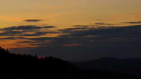 Side-movement-of-the-hilltops-where-dark-trees-are-hidden-in-the-background-of-shadows-and-silhouettes-of-clouds-moving-on-the-horizon-during-sunset