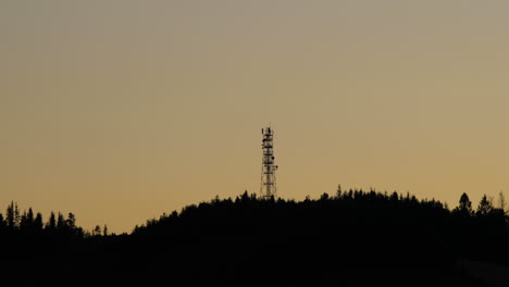 Blick-Auf-Die-Gipfel-Des-Hügels,-Wo-Der-Funkturm-Dunkle-Bäume-Ist,-Die-Im-Hintergrund-Von-Schatten-Und-Silhouetten-Von-Wolken-Versteckt-Sind,-Die-Sich-Während-Des-Sonnenuntergangs-Am-Horizont-Bewegen