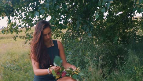 A-beautiful-young-girl-wearing-black-dress-and-arranging-flowers-and-leaves-around-the-tree-in-outdoors-during-visit-to-fields