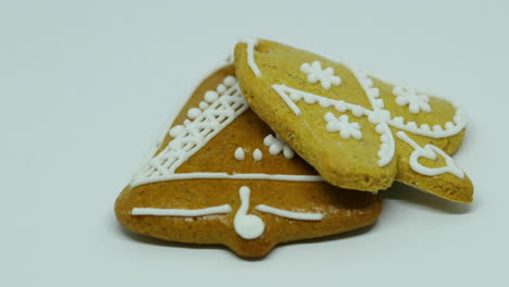 Side-slide-on-two-gingerbread-confectionery-with-white-decoration-on-top-in-the-shape-of-a-bell-and-heart-on-a-white-background