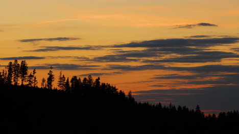 Side-movement-the-hilltops-where-dark-trees-are-hidden-in-the-background-of-shadows-and-silhouettes-of-clouds-moving-on-the-horizon-during-sunset