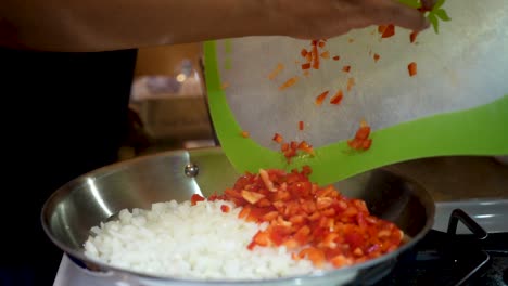 Dumping-diced-red-bell-peppers-into-a-skillet-with-fresh-onions-as-part-of-a-homemade-recipe---slow-motion
