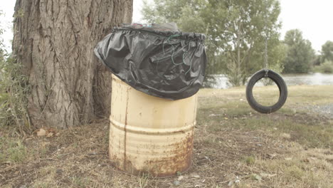 Trash-can-lonely-tire-swing-near-riverbank-in-Melnik,-wide-angle